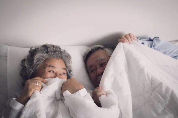 上了年纪的夫妇白头偕老 男女都睡在床上 在卧室的白色毛毯里笑着 退休后的医疗保健与爱情生活方式的概念 — 图库照片