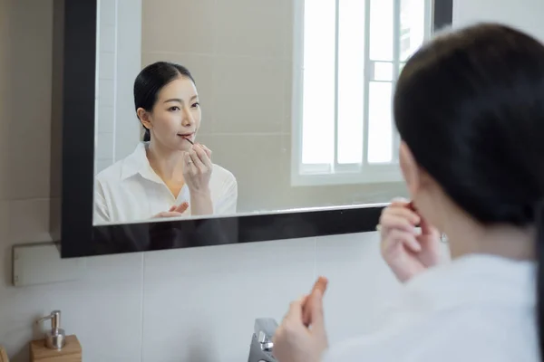 亚洲女人穿着白衬衫 在浴室的镜子前化妆 — 图库照片