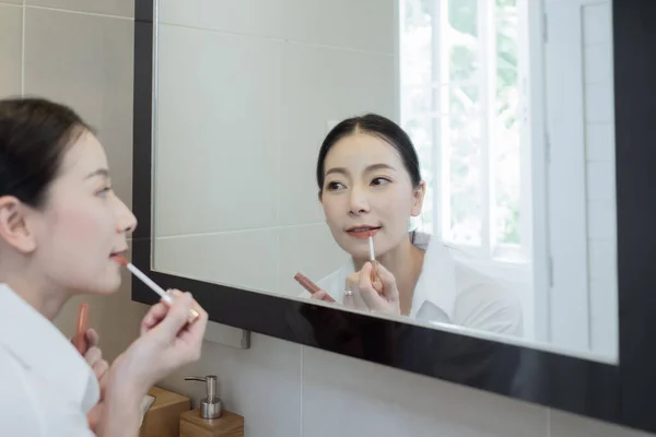 亚洲女人穿着白衬衫 在浴室的镜子前化妆 — 图库照片