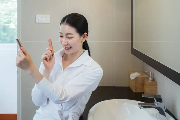 亚洲女人穿着白衬衫 在浴室的镜子前选择化妆 — 图库照片