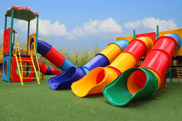 Renkli oyun parkı mavi gökyüzünde çocuklar, çiçek ve çimen arka planında mutlu ekipmanlar inşa etmektir.