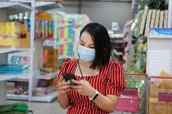 Genç kadınlar virüslerden korunmak için maske takarlar. Alışveriş merkezine git ve ürün listesini telefonla kontrol et..