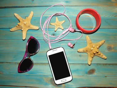 Akıllı telefon, kulaklıklar, bilezik ve güneş gözlüğü mavi ahşap yüzeyde. Yukarıdan görünüm.