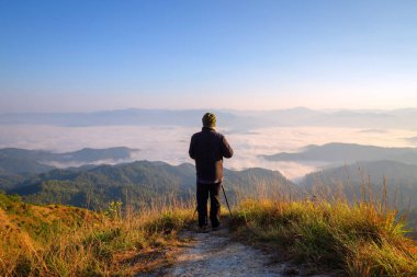 Elinde fotoğraf makinesi olan yürüyüşçü dağın tepesinde duruyor.