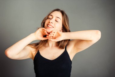 Saçları siyah bluzlu, elleri çenesinin altında gri arka planda bir kız. Makyajsız.
