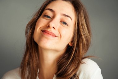 Gri arka planda beyaz gömlekli gülümseyen genç bir kızın yakın plan portresi. Ellerini yüzüne koy. rötuş ve makyaj olmadan.