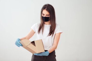 Paketi siyah maskeli ve mavi eldivenli bir kız açıyor. Karantina sırasında mesafeyi koruyor. Malların dünya çapında güvenli teslimatı.