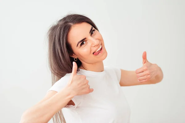 Atraktivní Bruneta Bílém Tričku Ukazuje Palce Nahoru Radostně Vyčnívající Jazyk — Stock fotografie