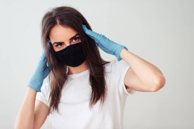 Siyah tıbbi maskeli bir kızın portresi ve beyaz arka planda beyaz tişörtlü, elleri kafasının yanında eldivenli bir kız. Soğuk algınlığının belirtileri. Evde kal konsepti