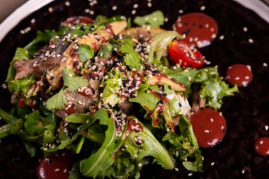 Arugula, domates ve et salatası siyah bir tabakta ve restoranda servis ediliyor.