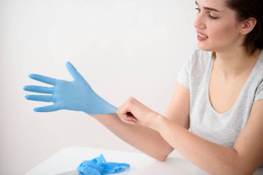 Kız, işten önce hafif bir arka planda masada otururken lastik eldiven takıyor. Karantina Güvenli Teslimat Konsepti