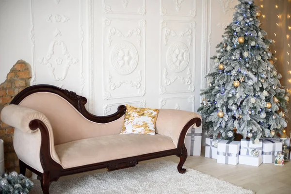 Festive Christmas living room or studio interior with a snowy Christmas tree, white gift boxes and a sofa.