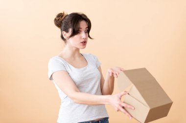 Şaşkınlık içinde toplanmış saçı olan kız bir karton kutuyu açıyor ve ona merakla bakıyor. Çantayı bej bir duvara boşalt.