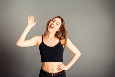 Siyah bluzlu, saçları sallanan ve gülümseyen gri arka planda bir kız. Makyajsız, rötuşsuz.