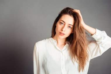 Gülümseyen kız, gri arka planda elleri yüzüne yakın, kapat. Makyajsız, rötuşsuz.