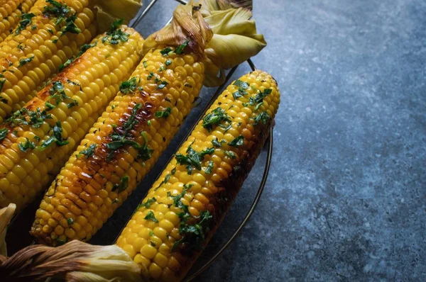 Native American cuisine, roasted corncobs with green herbs and sauce on blue marble background, close-up. Grilled corn, healthy eating concept. Selective Focus