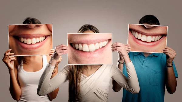 three happy people holding a picture of a mouth smiling on a gray background