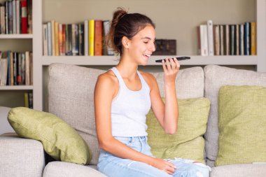 Mutlu genç kız evde bir kanepede oturmuş akıllı bir telefonla sesli mesaj yolluyor.