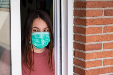 Evde kapalı kalmış tıbbi maske takan genç bir kadın. Coronavirus konsepti