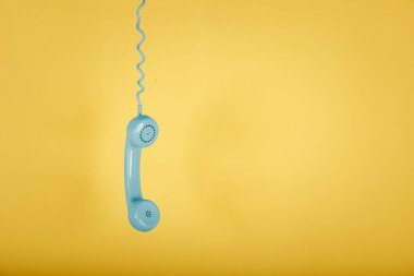 Sarı arka planda asılı mavi vintage telefon