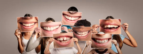 Bir grup mutlu insan ellerinde gri arka planda gülümseyen bir ağız resmi tutuyorlar.