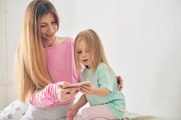 Mom and daughter using smart phone in bed