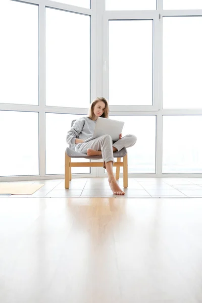 Woman in armchair working on laptop near panoramic window