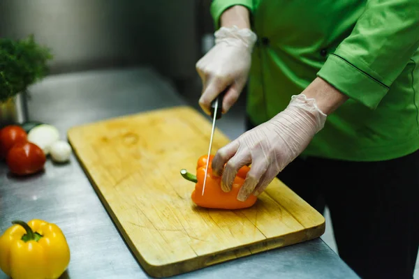 Повар в перчатках режет овощи на деревянной доске. профессиональная кухня со стальной столешницей — стоковое фото