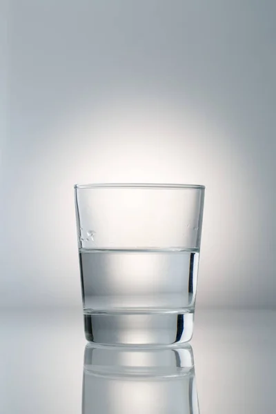 Vidro com água no fundo cinza claro gradiente — Fotografia de Stock