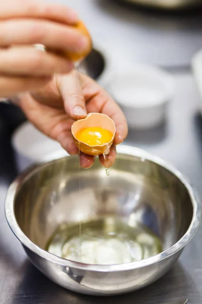 O cozinheiro quebra o ovo em uma tigela de aço — Fotografia de Stock