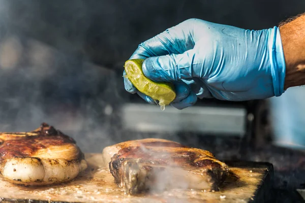 Aşçı biftek ızgara üzerine limon suyu sıkıyor. Taze, lezzetli ızgara et 