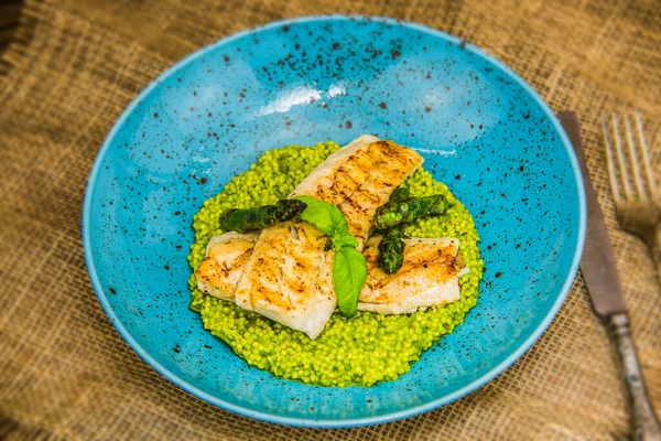 Tabakta yeşil kuskus ve taze kuşkonmaz ile kızarmış balık filetosu. Restorandaki yemek. Yemek tasarımı ve restoran yemeği.
