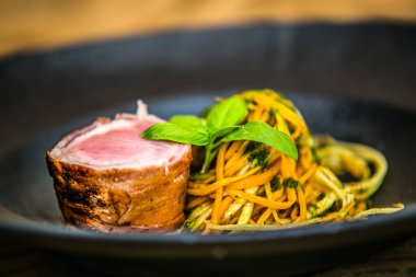 Domuz pastırmasına sarılı bonfile ve havuçlu erişte. Restorandaki yemek. Yemek tasarımı ve restoran yemeği.