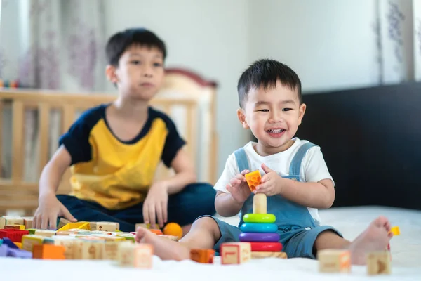 哥哥和一个微笑的男孩在床上玩玩具聚集 这个模仿可以用于孩子 家庭和玩具的概念 — 图库照片