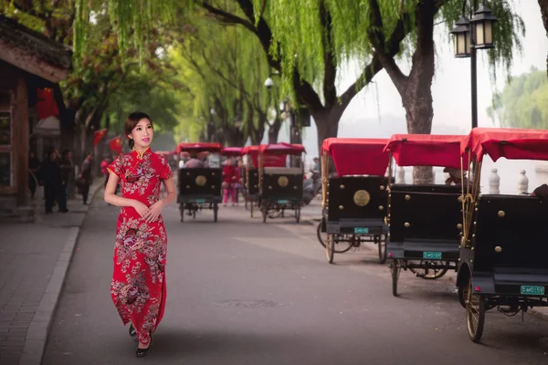 中国身着红色旗袍的中国女士走在中国北京老胡同的一位乘坐北京传统黄包车的游客附近 — 图库照片