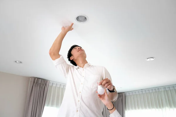 Power saving concept. Asia man changing compact fluorescent — Stock Photo, Image