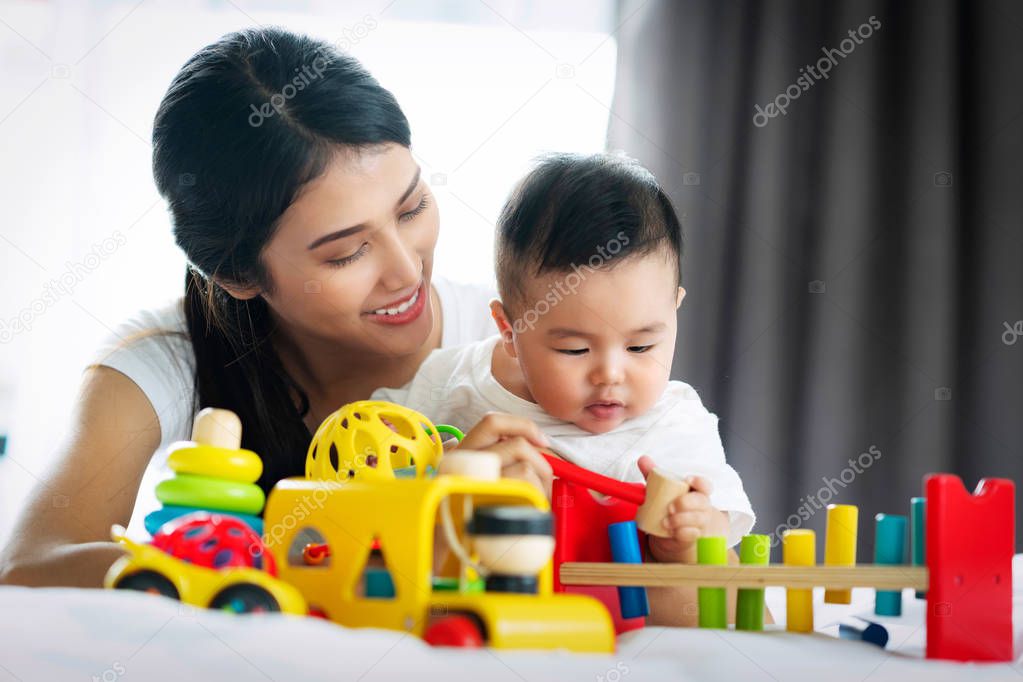 Asian mother and baby play togather with wooded toy in bed room