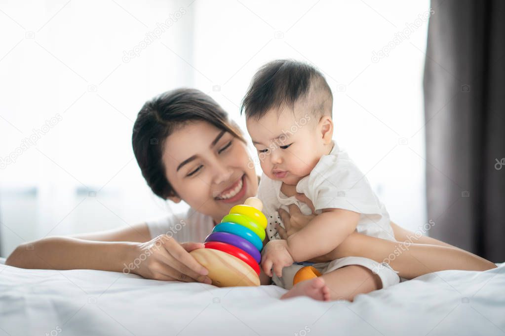 sian mother play with her baby in bed room