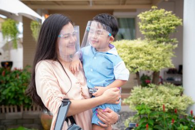 Coronavirus covid-19 concept.Little asian boy with mother wearing face shield mask for protect from coronavirus for back to school. School kid go to school with mom.New normal lifestyle post coronavirus.