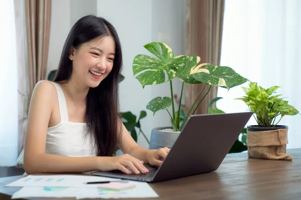 テーブルの上に緑の植物と木製のデッキに彼女のレポートを準備するために彼女のコンピュータノートブックにデータを入力するアジアの女の子 この画像は 教育のために使用することができます オフィス 大学や学生の概念 — ストック写真