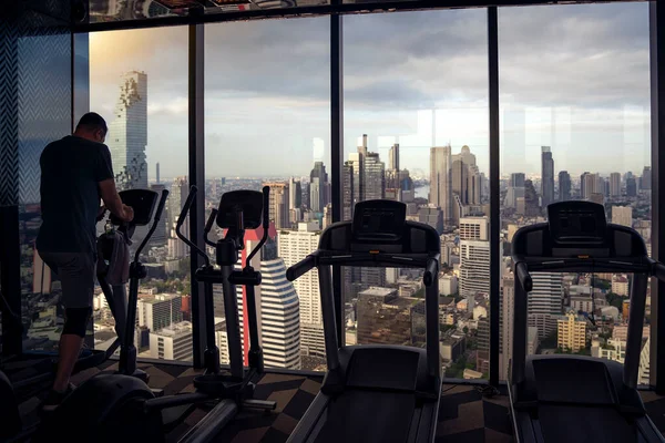 A man on fitness equipment in fitness club with Bangkok city view background from the vindows