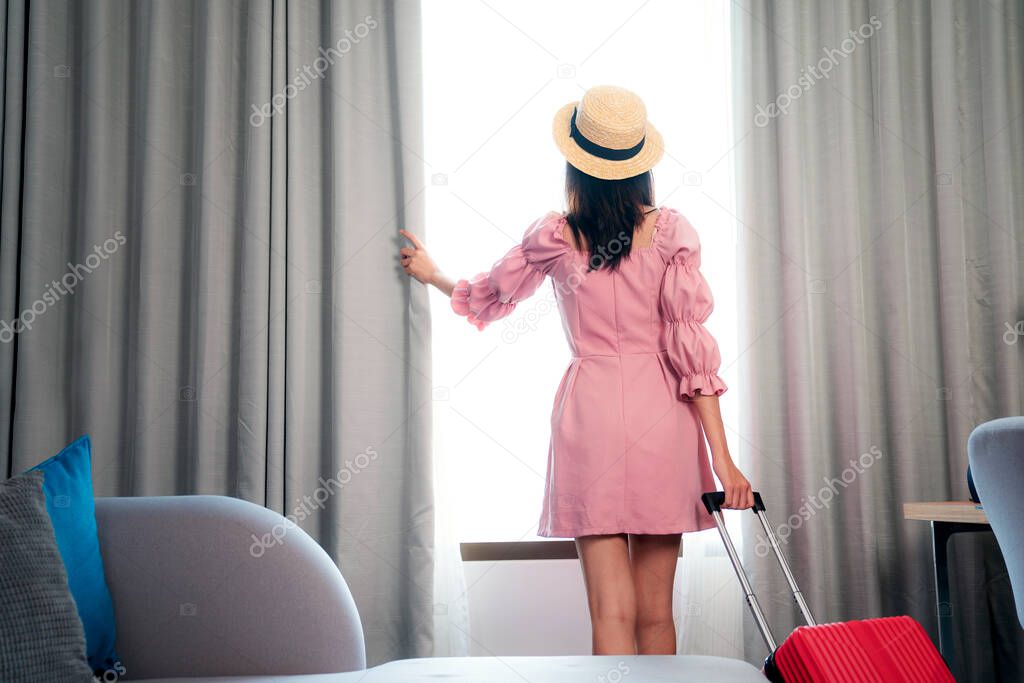 Asian woman traveller in pink dress arrive to room in hotel and open curtain for enjoy with outside view, this image can use for Travel, tour, hotel and travel insurance concept