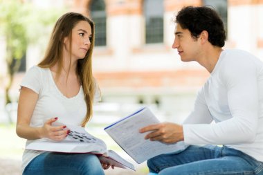 İki öğrenci açık hava bankında birlikte ders çalışıyor.