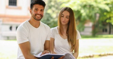 İki öğrenci açık hava bankında birlikte ders çalışıyor.