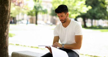 Yakışıklı genç adam parkta bankta kitap okuma