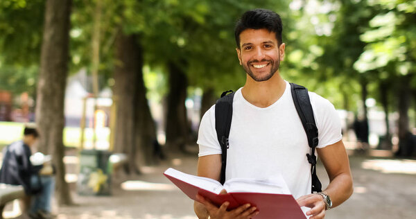 Красивый молодой человек читает книгу во дворе колледжа
