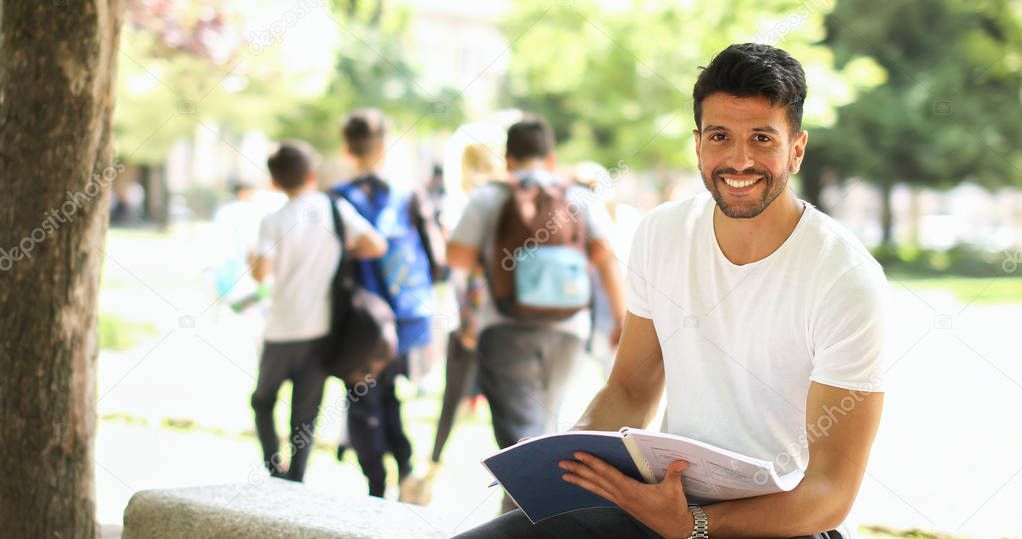 Handsome young man reading book on bench in the park