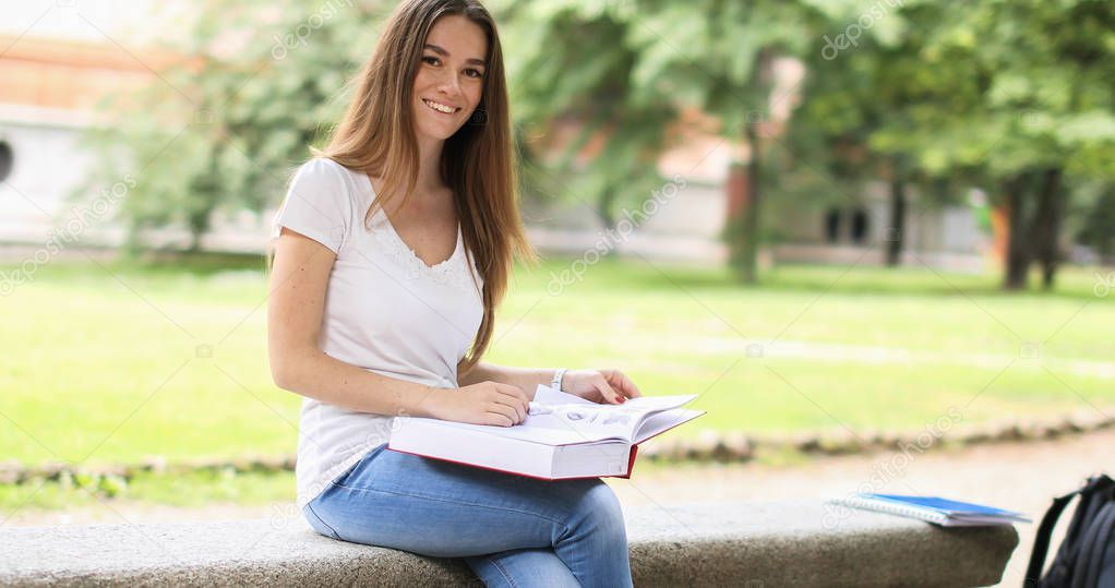 Beautiful female college student reading a book on a bench in a park