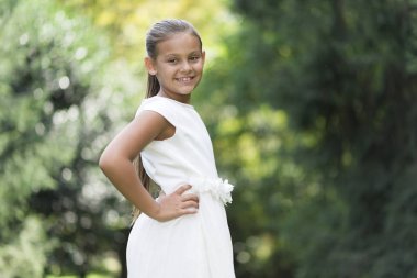 Güzel kız açık havada beyaz elbise ile gülümseyen kalçalarına eller 