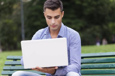 Genç adam açık havada bir dizüstü bilgisayar kullanarak